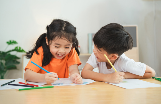 Two children are sitting at a table, drawing and smiling. Concept of joy and creativity, as the children are engaged in a fun activity together
