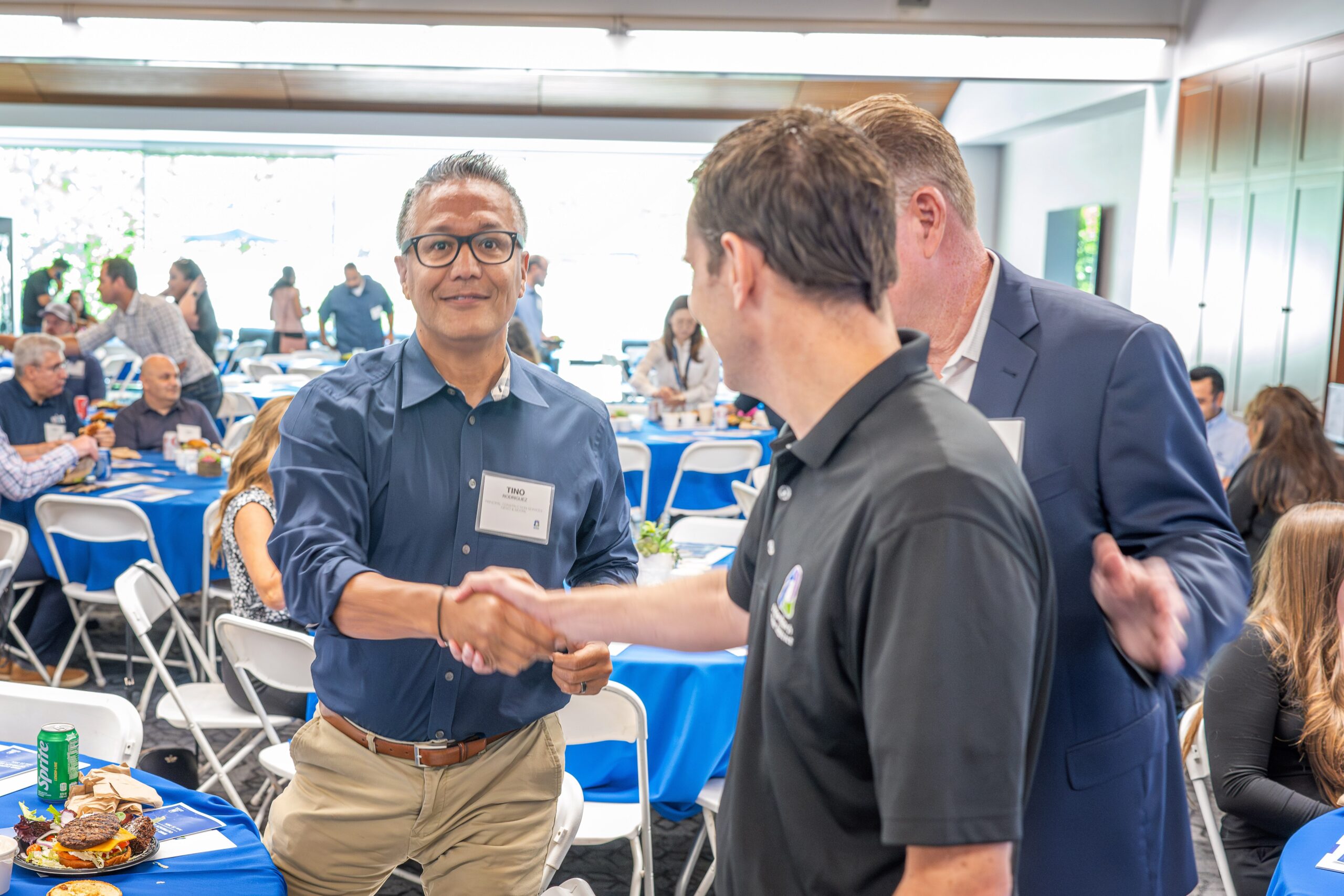 Attendee in blue shirt and glasses shakes hands with a colleague at a conference reception.