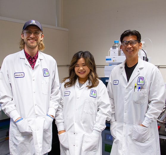 Three researchers in white lab coats pose in a modern laboratory with equipment in the background.