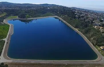 Aerial view of a large rectangular man-made reservoir surrounded by a looping road and hillside houses.