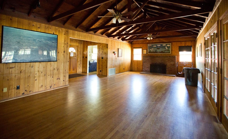 Spacious rustic living room with wood-paneled walls, exposed beams, and a brick fireplace.