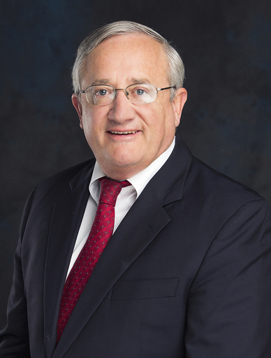 Senior man in a dark suit and red tie posing in a studio portrait.