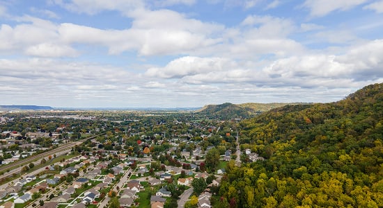 Aerial view of a suburban neighborhood beside a forested hill under a cloudy sky.