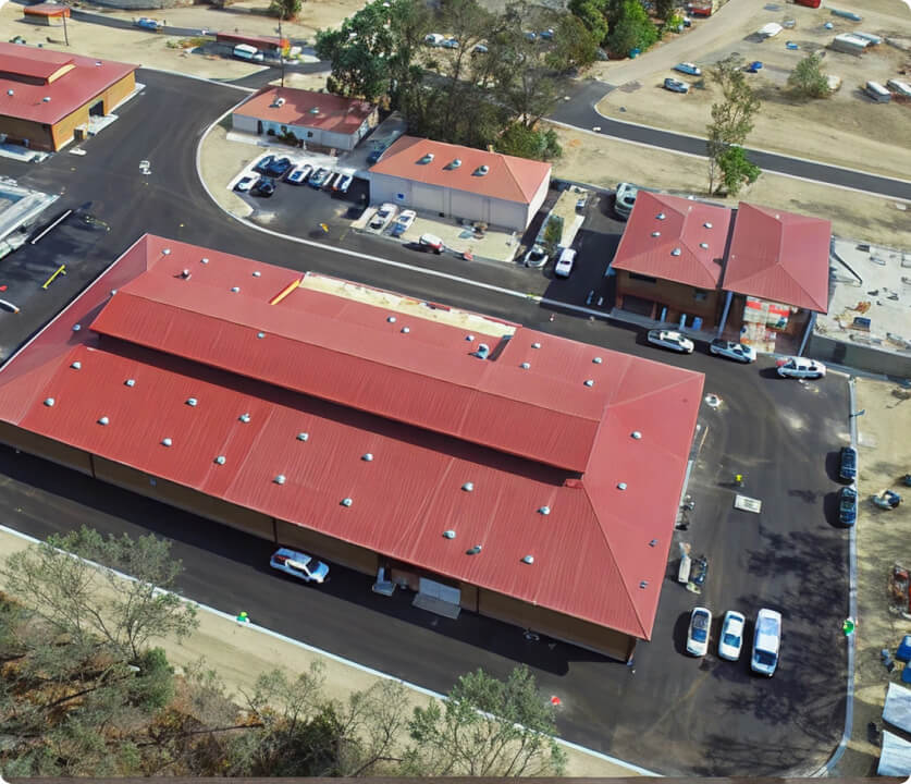Aerial view of a red-roof shopping plaza with parking and surrounding roads.