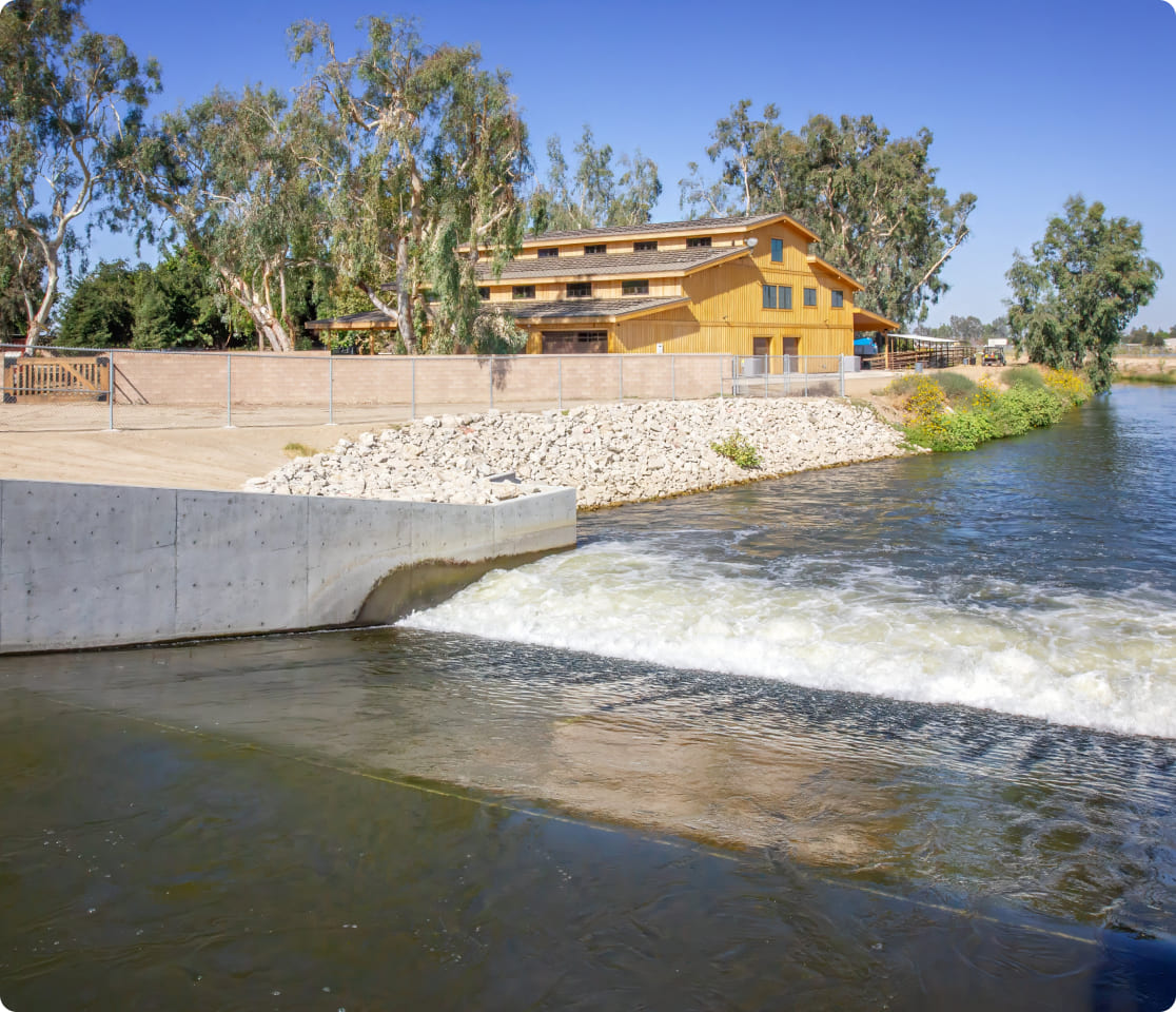 Wooden riverfront building beside a spillway dam with trees and blue sky.