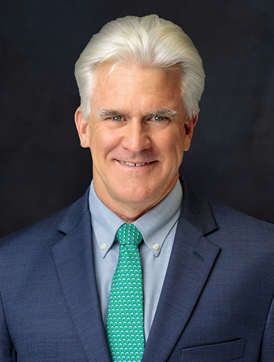 Professional portrait of a smiling man in a navy suit and teal patterned tie.