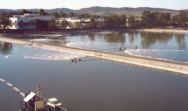 Wastewater treatment plant with rectangular basins, walkways, and distant hills.