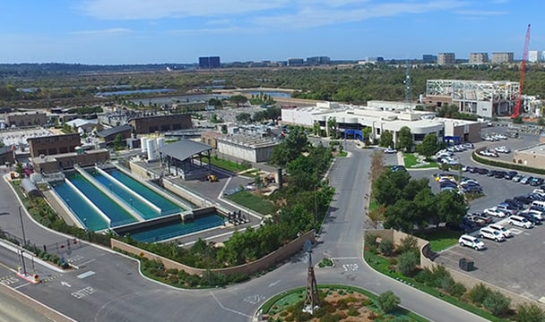 Aerial view of a mixed-use campus with outdoor swimming pools, modern buildings, and surrounding roads.