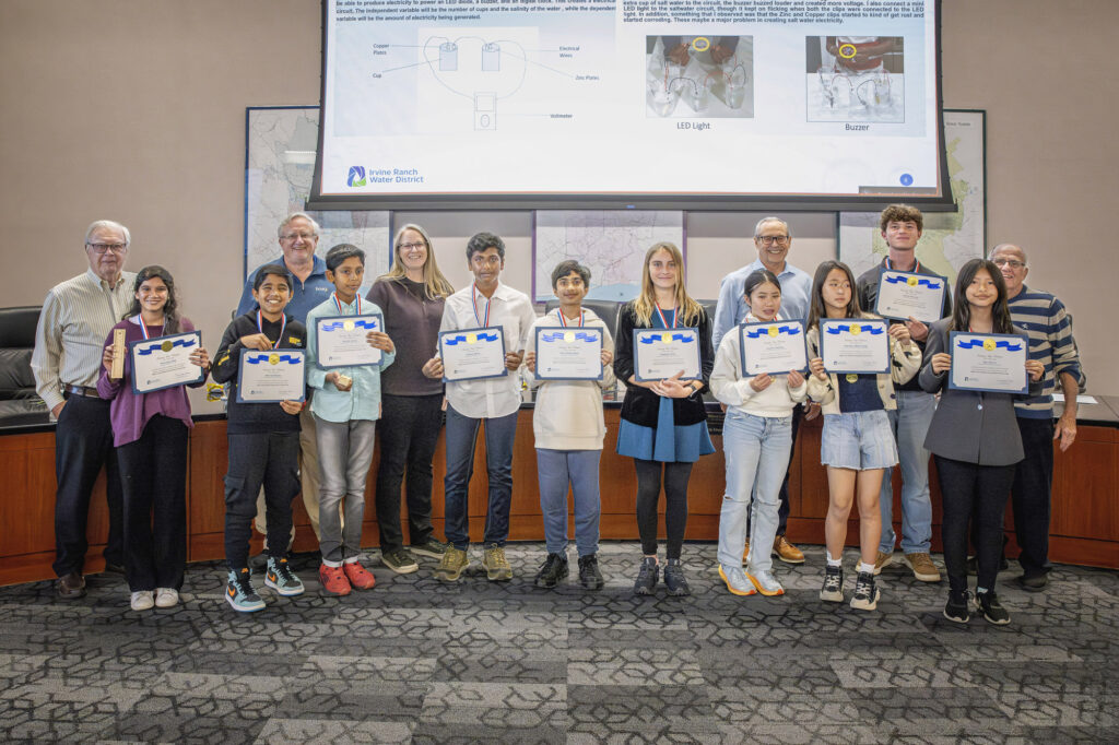 Group of diverse students and adults pose with certificates and medals at an Irvine Ranch Water District awards ceremony.