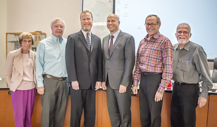 Six adults in business attire stand together in a wood-paneled conference room, smiling at the camera.