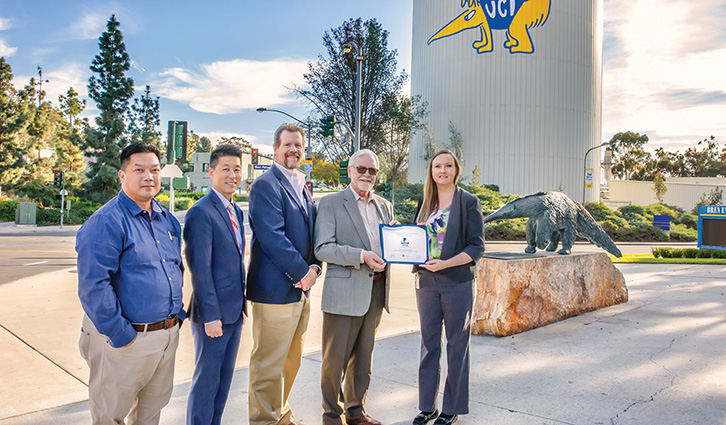 Group of professionals outdoors presenting a framed certificate beside a dinosaur sculpture.