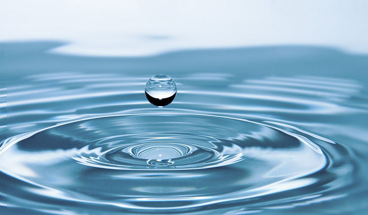 Water droplet hovering above rippling blue water surface.