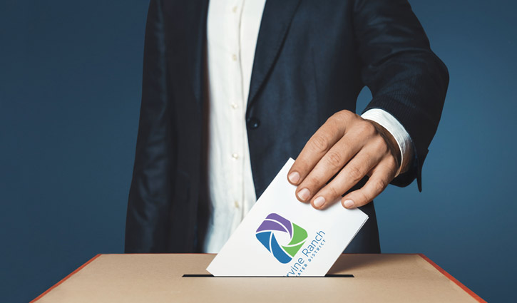 Person in a dark suit inserts a ballot into a wooden ballot box.