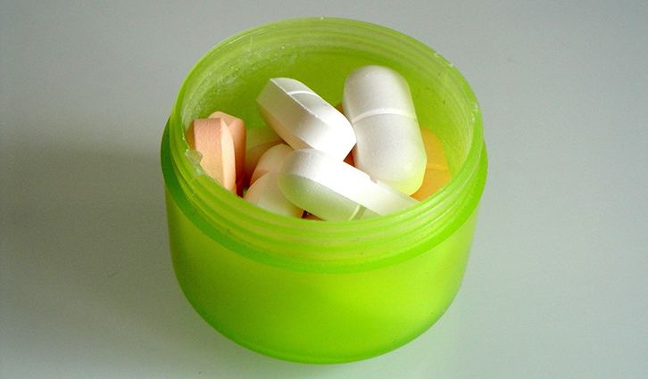 Open green pill bottle filled with white tablets and pink pills