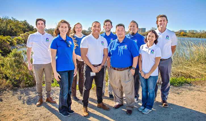 Group of diverse professionals posing outdoors by a lake in matching polo shirts with logos.