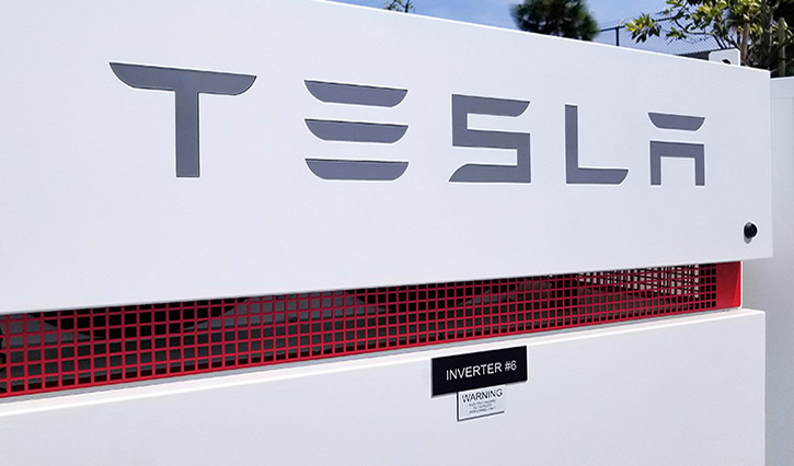 Close-up of a Tesla inverter unit with a white panel, red vent grille, and the Tesla logo.