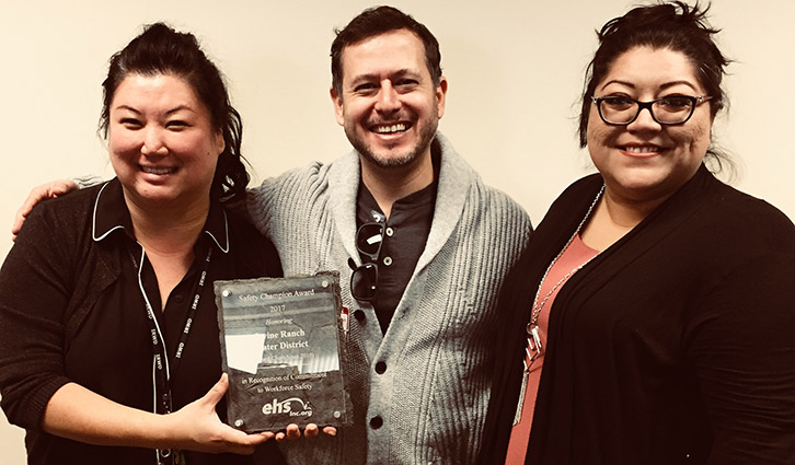 Three coworkers pose together, smiling, while holding a Safety Champion Award plaque.