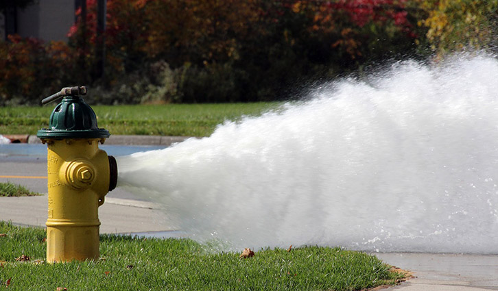 Yellow fire hydrant spraying a wide jet of water across a sidewalk