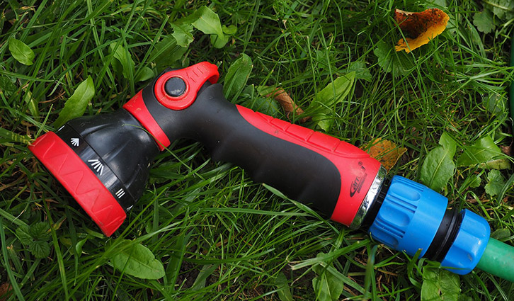 Red and black ergonomic garden hose nozzle with blue quick-connect fitting lying on green grass.