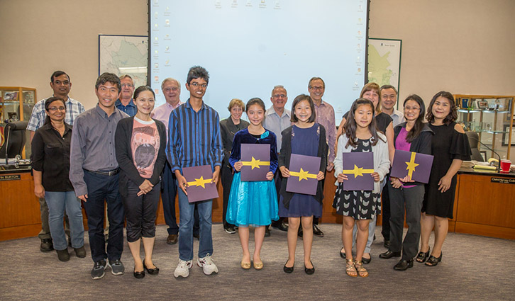 Group of students and adults posing with certificates in a classroom during an award ceremony.