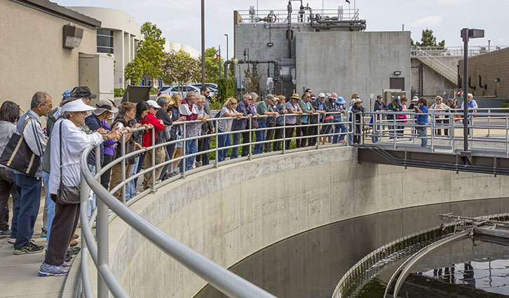 Group of visitors lined up along a curved railing at a wastewater treatment plant tour.