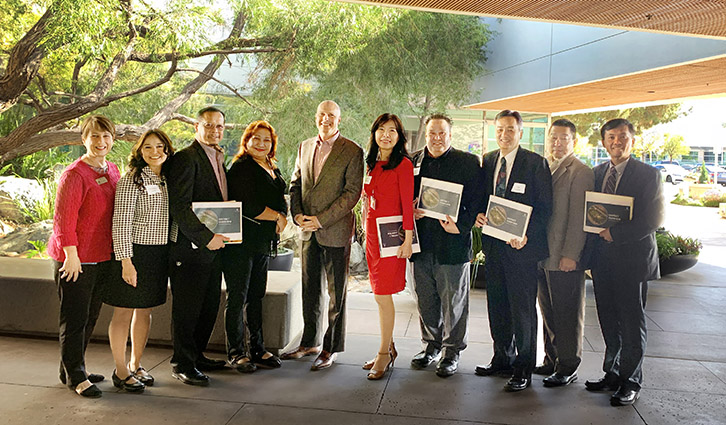 Group of professionals standing outdoors, each holding a certificate or booklet.