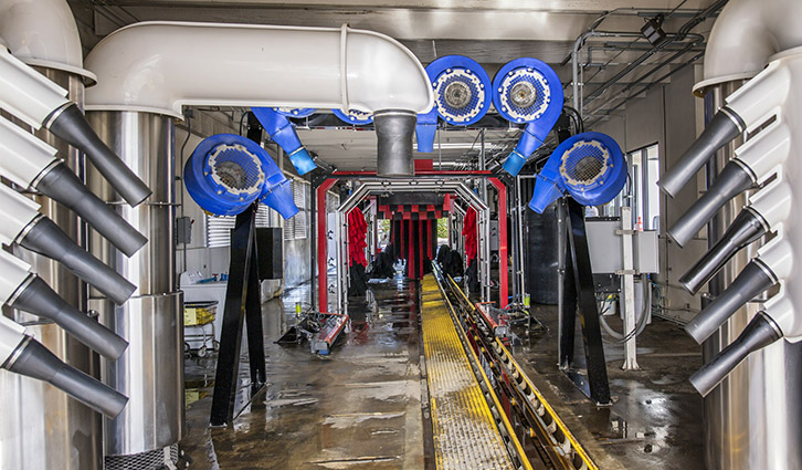 Automated car wash tunnel with multiple spray arms and a wet floor.