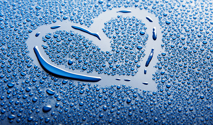 Blue surface covered with water droplets arranged to form a heart.