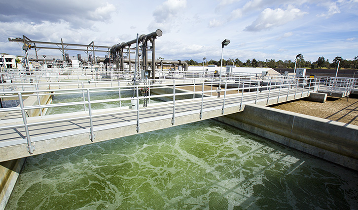 Wastewater treatment facility with aeration tanks, metal walkways, and foamy green water.