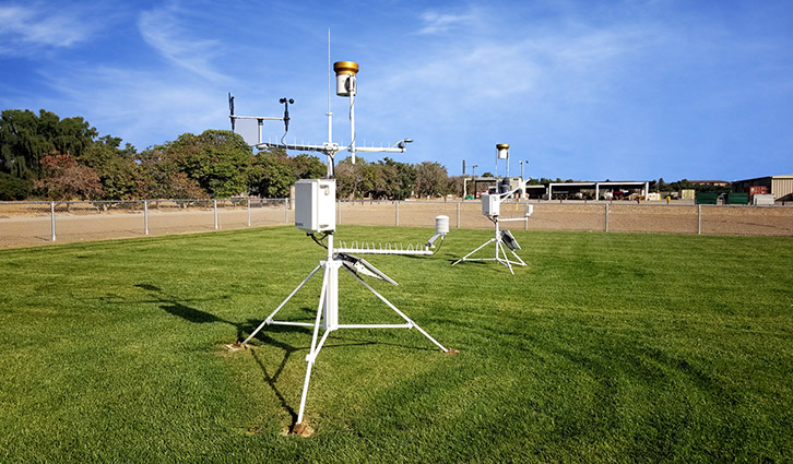 Weather monitoring station with sensors on tripods in a grassy field.