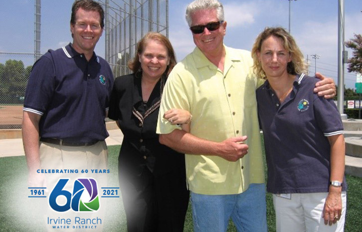 Group of four adults posing outdoors beside a sports field, with an Irvine Ranch Water District 60th anniversary logo.