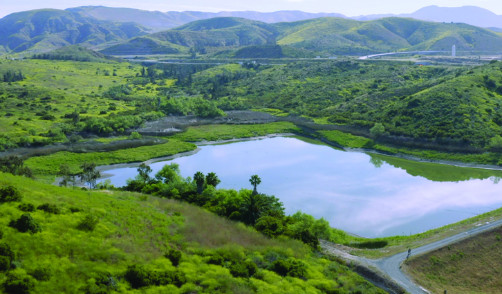 Lush green valley with a reflective blue lake framed by rolling hills and distant mountains