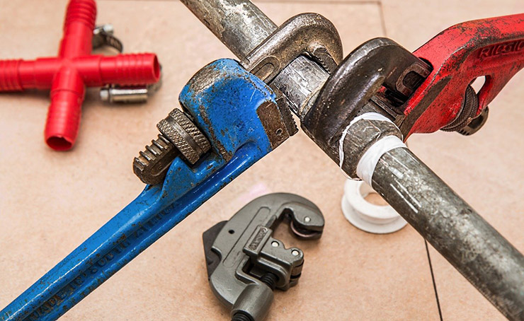Close-up of blue pipe secured by a metal clamp, with fittings and a red wrench in the background.