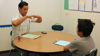 Instructor demonstrates a technique to a student at a round table in a classroom.