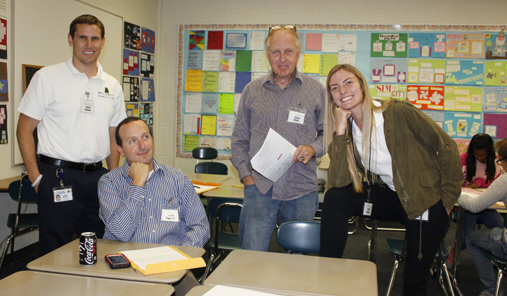 Four adults posing in a classroom with colorful student posters on the wall.