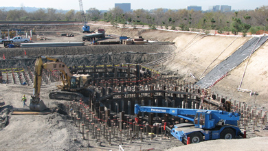 Circular underground foundation pit under construction with formwork, steel shoring, and heavy machinery on site.