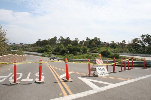 Road closed with orange traffic cones and a 'Road Closed' sign across a bridge.