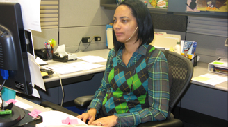 Woman in a plaid green and blue shirt sits at a desk in a modern office.