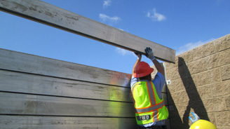 Construction worker in a neon safety vest and red hard hat lifting a wooden beam at a construction site