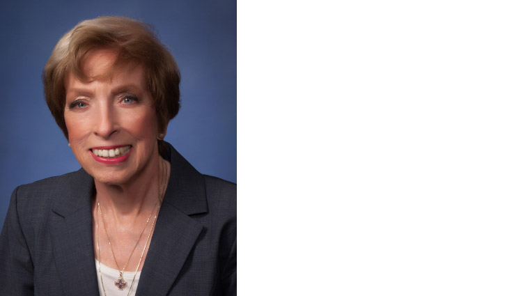 Smiling professional woman in a dark blazer against a blue studio backdrop.