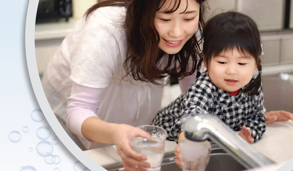 A woman helps a young girl wash a glass at the kitchen sink.