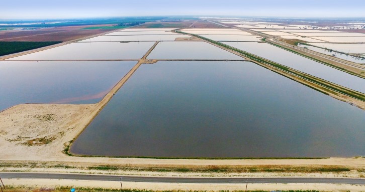 Aerial view of rectangular salt evaporation ponds separated by dirt embankments along a coastline.