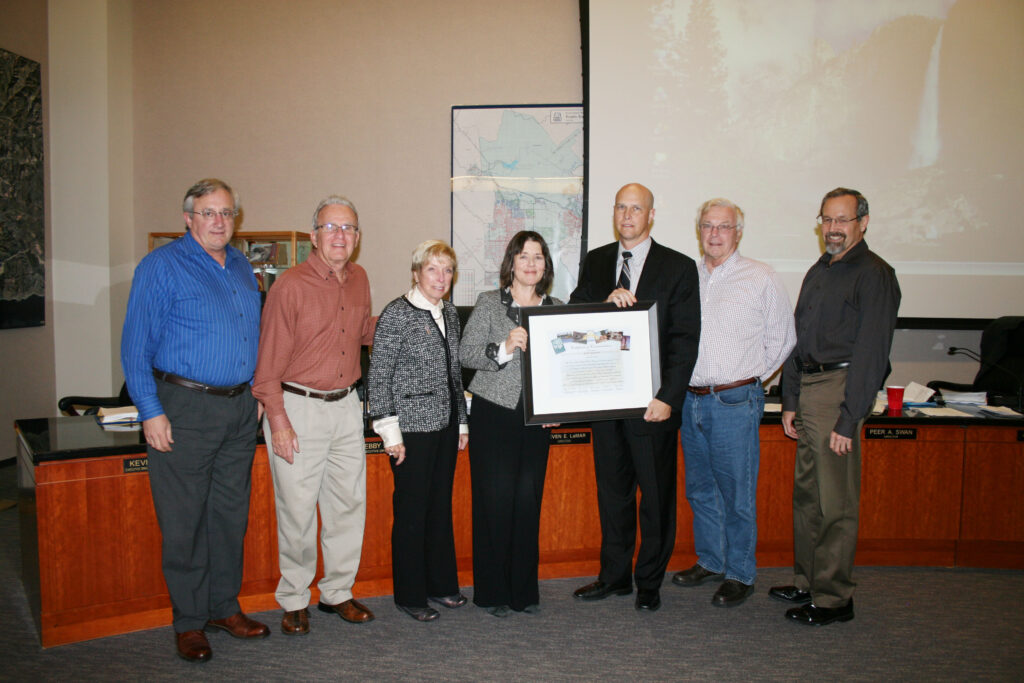 Seven professionals stand in a conference room, posing with a framed certificate during an award presentation.