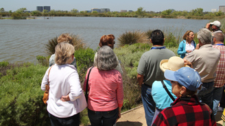 Tour group standing by a riverside, facing away from the camera.