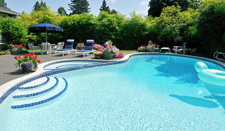 Backyard swimming pool with curved blue-tiled steps, surrounded by lounge chairs, an umbrella, and colorful flower planters.
