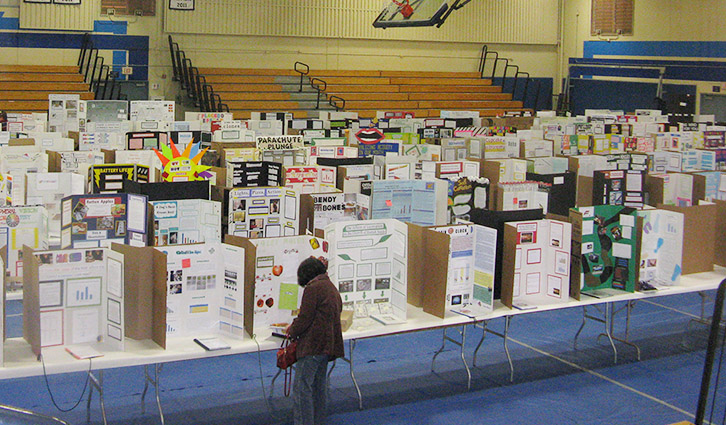 Student browses science fair projects set up on display boards in a gymnasium.