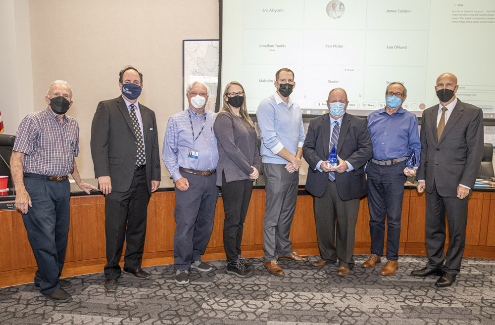 Group of professionals in a conference room wearing masks, posing with glass awards during a ceremony.