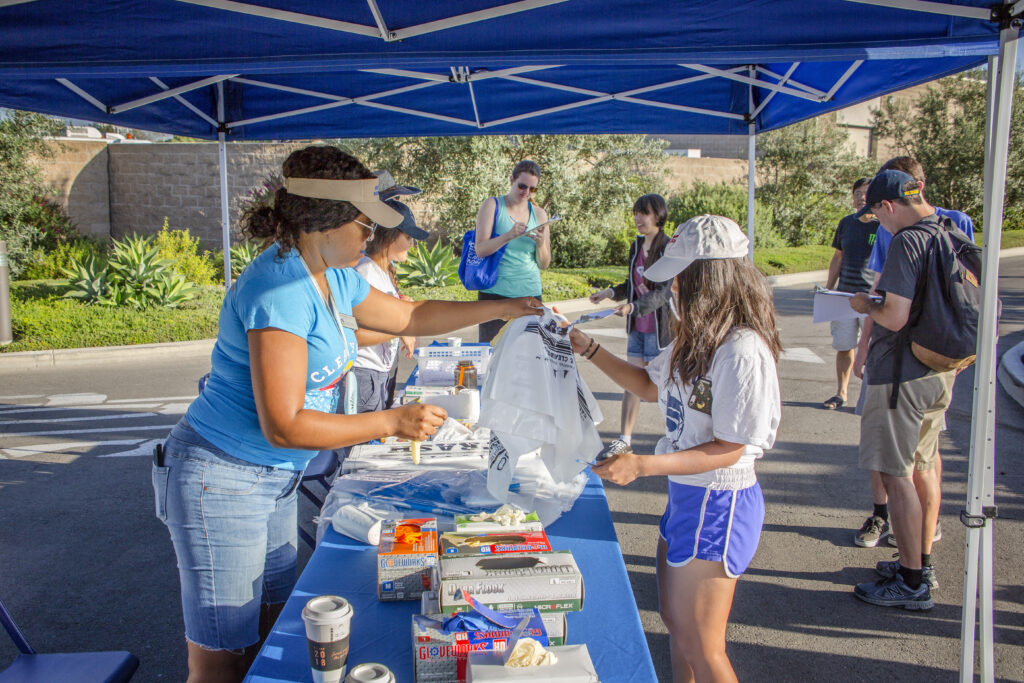 Volunteer hands a bag to a participant at an outdoor community event under a blue canopy.