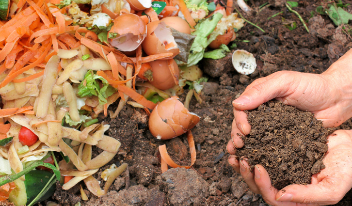 Hands holding compost soil beside kitchen waste including eggshells and vegetable peels.