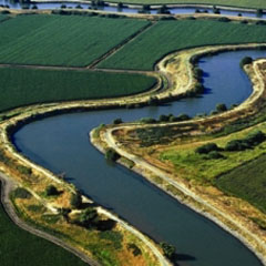 Aerial view of a winding canal weaving through emerald farmland.